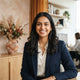 A friendly South Asian woman smiling in a bright office space.